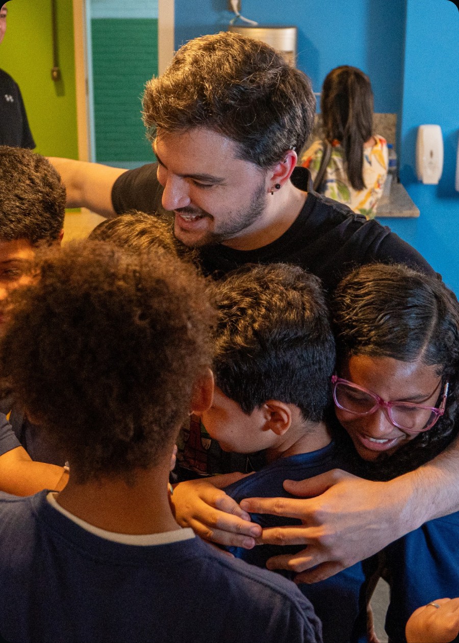 Educador abraçado por um grupo de crianças em uma atividade da Fábrica Social
