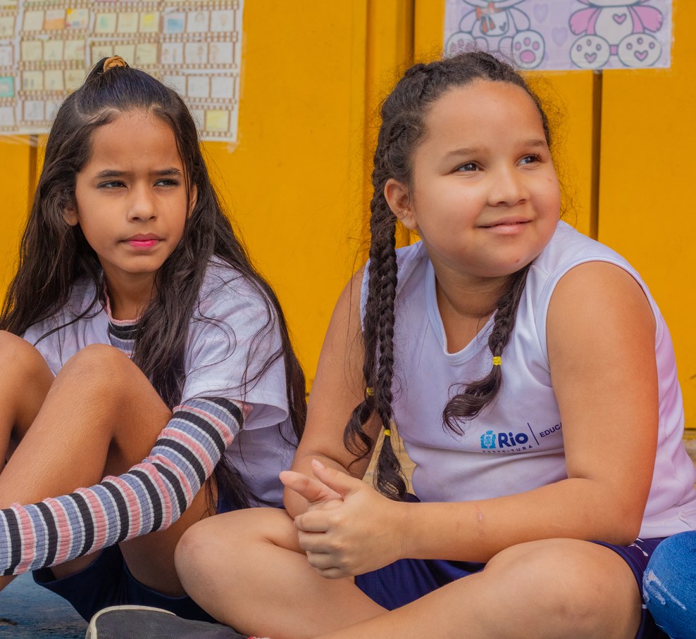 Duas meninas em uniforme escolar sentadas em frente a um mural de desenhos