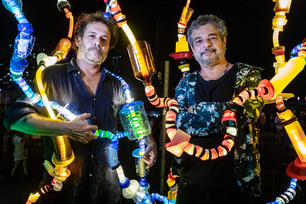 Dois artesãos ao lado de esculturas luminosas feitas de garrafas PET
